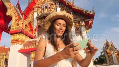年轻的高加索旅游妇女在泰国佛寺用手机拍摄自拍照片。 泰国普吉岛。 4K