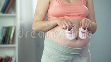 孕妇怀宝宝，在大肚子上玩婴儿鞋，快乐