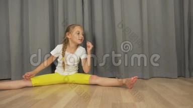 小女孩坐在客厅的地板上。 白人女孩伸展和跳舞。 女孩在室内分开。