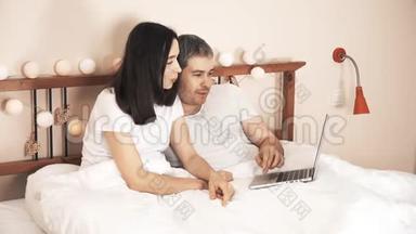 幸福夫妻在家里床上用笔记本电脑上网购物