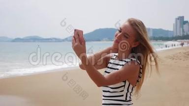 年轻漂亮的苗条女人，一头金发，穿着黑白连衣裙，在海边的手机上自拍