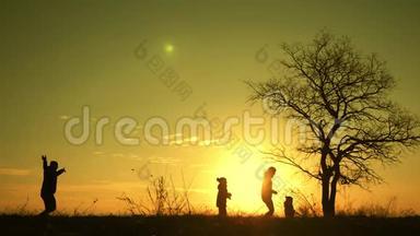 日落时，幸福的家庭在一棵<strong>大树</strong>附近的草地上散步的<strong>剪影</strong>。