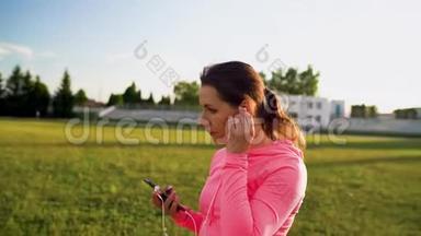 三合一视频。 日落时分，戴着耳机和智能手机的女人穿过体育场