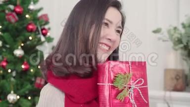 圣诞<strong>佳节</strong>，快乐的年轻亚洲女人在家的客厅里，捧着圣诞礼物微笑着拍照。