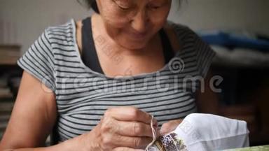 幸福老年妇女缝纫十字绣图案在白棉帆布上。 4K，慢动作。