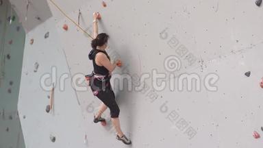 年轻女子在室内攀岩墙上锻炼。 在攀岩墙上训练登山者。 女孩锻炼了摇滚