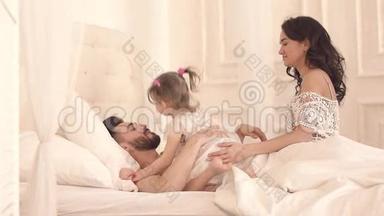 在阳光明媚的早晨，幸福的一家人在床上互<strong>相拥</strong>抱