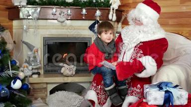 男孩坐在圣诞老人`腿上，孩子在信封里给圣尼古拉斯他的圣诞愿望单
