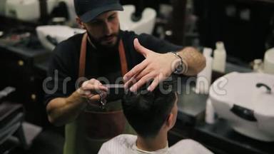 理发店里坐在椅子上理发的一位男客户，身穿围裙梳头的胡子理发师。 时尚