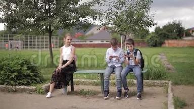两个男孩和女孩在放学后使用他们的电话。 可爱的男孩坐在长凳上玩网络游戏