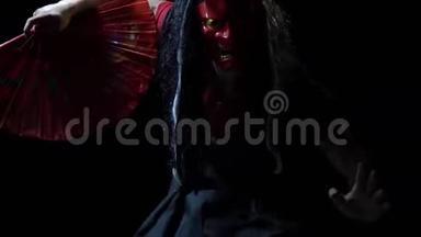 戴着日本<strong>恶魔</strong>面具，穿着<strong>黑色</strong>和服的怪物用一把红扇子遮住了他的脸