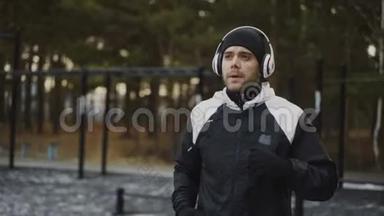 有魅力的男士戴着耳机做<strong>热身运动</strong>，准备在冬季公园听<strong>音乐</strong>时慢跑