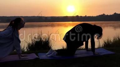 两名年轻女子<strong>四人</strong>站立，在日落的湖岸上训练呼吸