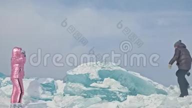 在冰封的湖面上，年轻夫妇在冬天散步时玩得很开心。 情侣们坐在蓝色的大冰块上