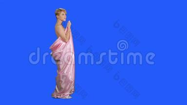穿着粉红色缎子床单的漂亮女孩在蓝色背景下摆着相机