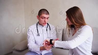 男医生向病人解释如何使用智能手表来监测健康，并坐在医院`办公室的沙发上。