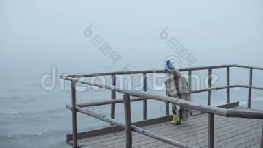 小女孩穿着橡胶靴和格子呢站在靠近大海的<strong>木墩</strong>上。 在多雾的风天里独自一个孩子。