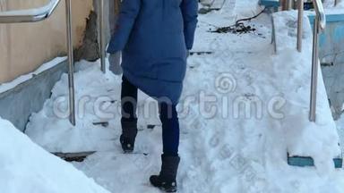 滑的楼梯。 一个穿着蓝色羽绒服的女人走在街上一个下雪的楼梯上。