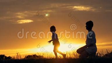 一个快乐的小男孩的剪影跑进他慈爱的母亲的怀里，在夕阳面前拥抱。