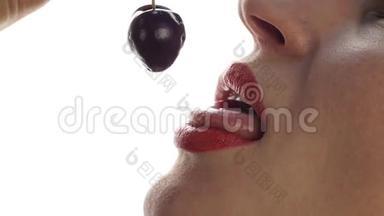美丽的女人舔和吃樱桃在白色的背景。 特写女孩咬樱桃。 慢动作