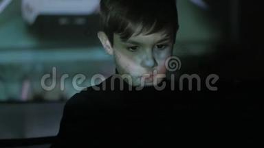 小男孩在黑暗<strong>的</strong>房间里用笔记本电脑玩电子<strong>游戏</strong>。 双曝光<strong>游戏的</strong>脸和墙上。