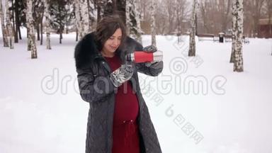 怀孕的女孩在冬季公园喝茶。