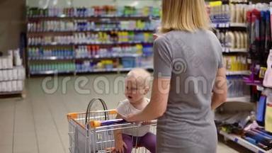 年轻的母亲带着她的小婴儿坐在超市的购物车里<strong>正向</strong>前走。 孩子在看