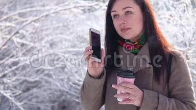一个年轻的女孩，穿着外套，漫步在冬季公园，写留言，喝咖啡