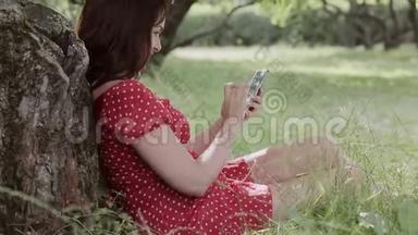 加上坐在树下的草地上的大小女孩使用她的智能手机