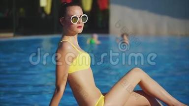 在游泳池附近阳光下晒太阳的身材好的女孩，炎热的夏天天气
