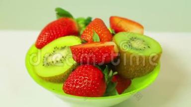 鲜奇异果和切片草莓在蓝色背景上的绿色盘子旋转成一个圆圈。 从上面看。
