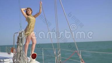 阳光明媚的一天，一金发美女站在一艘游艇的边缘，在阳光明媚的日子里在海上滑行，手里拿着