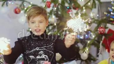 快乐的男孩在圣诞树上的bokeh灯和花环之间燃烧着火花。 慢动作。 3840x2160