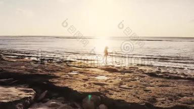 在美丽的日落中，站在海滩上观看海景的年轻有思想的女人