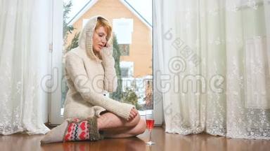 穿着毛衣的漂亮女人坐在靠近窗户的地板上打电话
