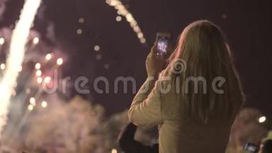 女孩在智能手机上射击敬礼。 年轻女孩在智能手机上拍摄烟花。 城市假日，