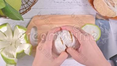 年轻的亚洲妇女正在剥鲜<strong>蜜柚</strong>，在明亮的白色木桌和砧板上的家庭厨房里吃，顶部的景色。