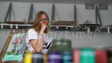 一位年轻迷人的艺术家，手里拿着一把刷子，脸上画着一张脸，站在画架上。