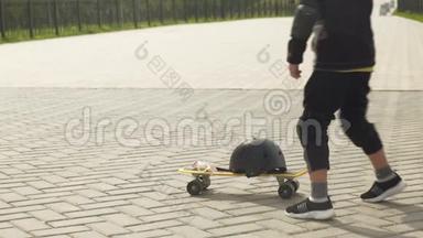一个带防护头盔的学龄前男孩在公园里骑滑板。 夏季