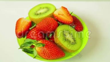 鲜奇异果和切片草莓在蓝色背景上的盘子旋转成一个圆圈。 从上面看。