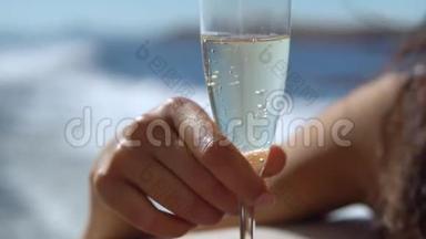 年轻的女人拿着一杯香槟，美丽的晒黑的女人手和一杯精致的饮料，近距离<strong>缓慢缓慢</strong>的动作，一个