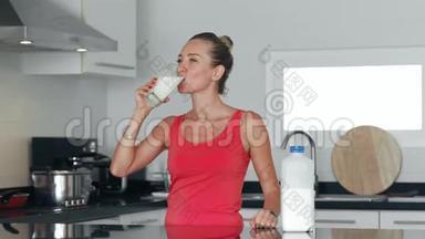 <strong>健康</strong>的女人从厨房的玻璃杯里喝牛奶，把牛奶瓶放冰箱里