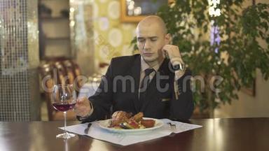 漂亮的聪明的秃头男人穿着经典的西装，在高档餐厅里独自看着一杯红酒品尝饮料