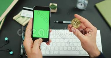 男人拿着一部黑色智能<strong>手机</strong>，绿色屏幕覆盖着一张工作桌和一个<strong>金色</strong>的比特币