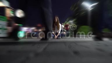 晚上，一个穿着衬衫和牛仔裤的女孩坐在广场中央，人们在那里散步和微笑，镜头模糊