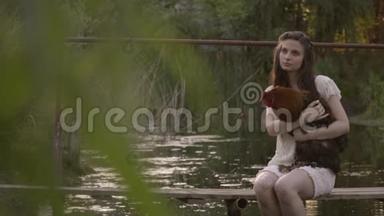 美丽的<strong>农村</strong>女孩穿着白色蕾丝连衣裙坐在河边的木桥上抱着公鸡，平静的<strong>农村生活</strong>在大自然中