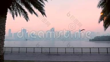 海鸥在码头堤岸水岸上缓慢飞行。 地平线上蓝雾的栅栏和建筑物。