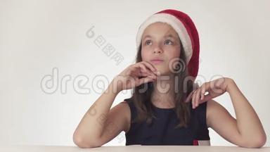 美丽的少女戴着圣诞老人的帽子梦想着礼物，收到想要的礼物，在白色背景下兴奋不已