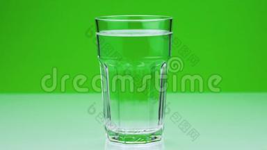 一片止痛的泡腾片落入玻璃杯中，在一片绿色的阿司匹林上溶解特写慢镜头