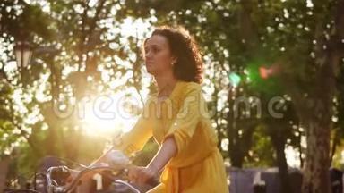 镜头耀斑：穿着黄色长裙的年轻女子骑着一辆城市自行车，车上有篮子，公园里有绿色的